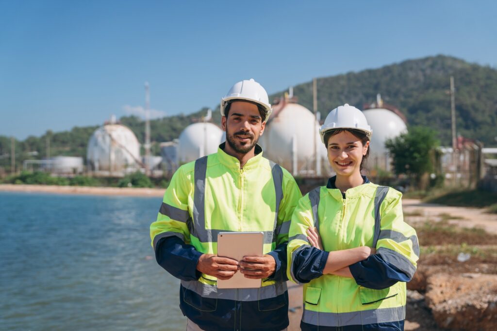 Smiling male and female engineering professionals holding a tablet at a petrochemical storage.